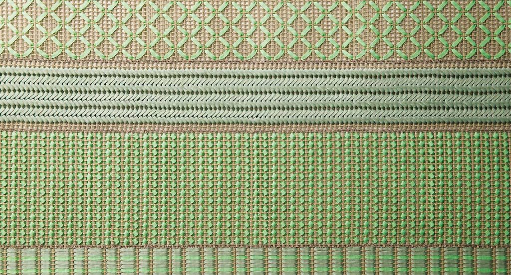 Grafismi modular rug. The geometric pattern is embroidered with green and brown flat braids in Rope yarn on kimia fabric.