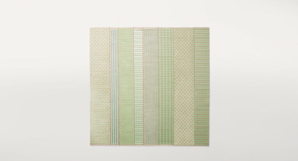Grafismi modular rug. The geometric pattern is embroidered with green and brown flat braids in Rope yarn on kimia fabric on a white background.