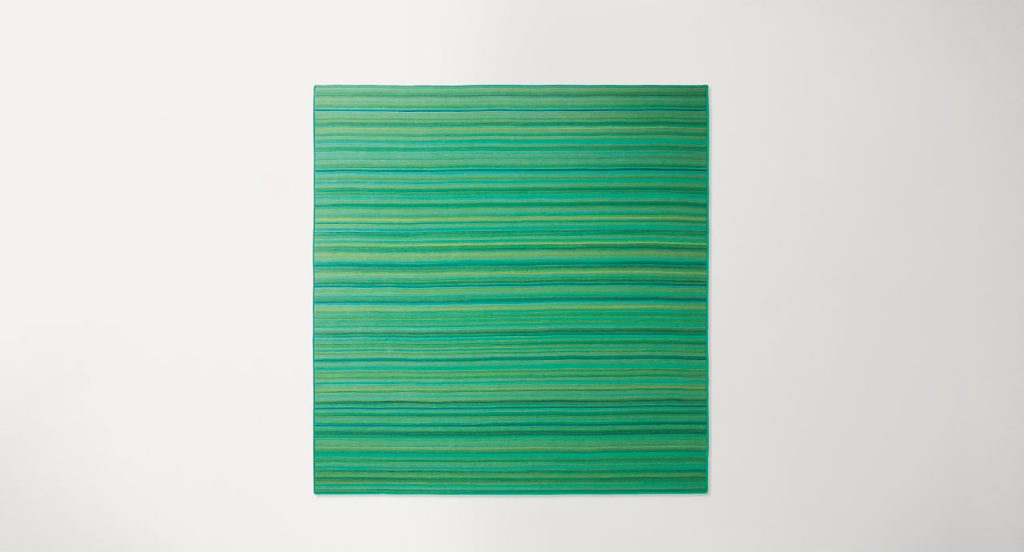 Parallelo rug made of blue and green wool cords on a white background.