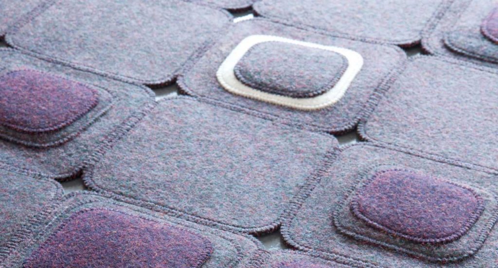 Pixel rug made with square felt elements in color purple and white on a white background.