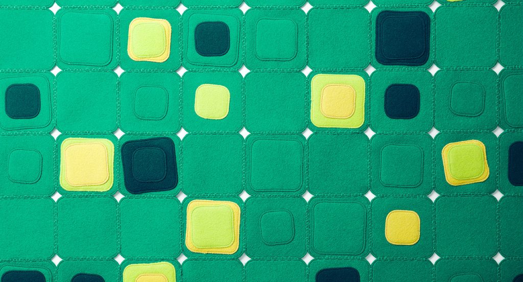 Pixel rug made with square felt elements in color blue, green and yellow on a white background.