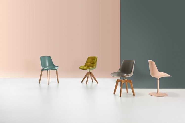 Four Flow Chair Colors , one color in light blue with four legs in natural oak cross base, one in light green with four legged cross in natural oak base, one in gray with four legged cross in natural oak base and one in powder pink with a central leg on a office background.