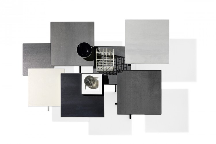 Seven K Tables, six tabletops in grey ceramic and frames in black steel, one tabletop in white ceramic and white steel on a white background.
