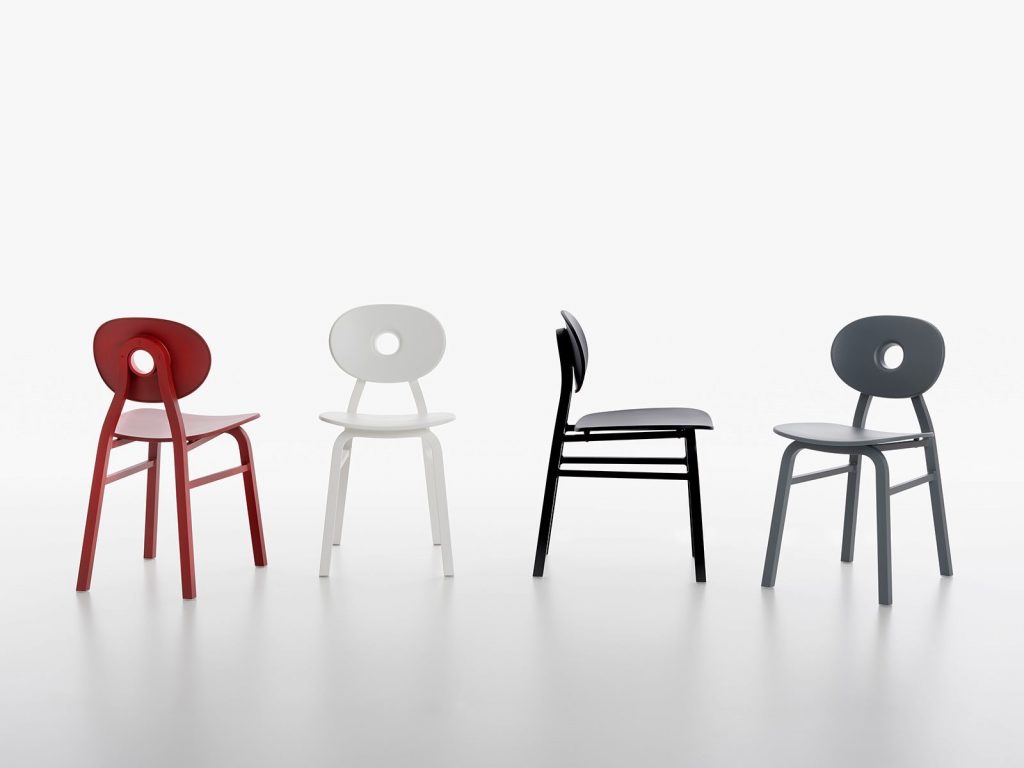 Four Elipse chairs, one in black, one in gray, one in red and one in white with round back with four legs in a dining room.