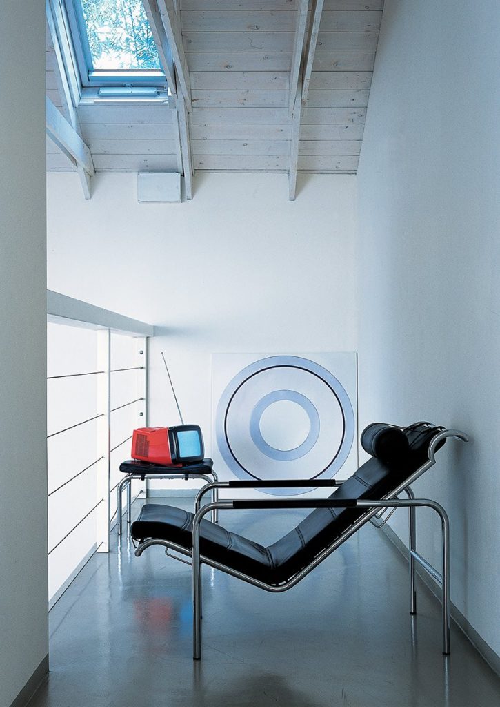 Genni lounge chair with a contemporary design, featuring a wide, black cushioned seat and a metal frame in a balcony.