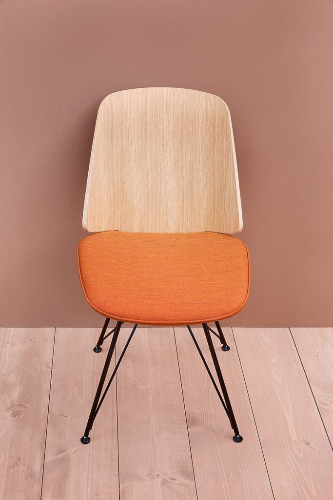 June chair with a orange cushioned seat and natural wood backrest on a brown background.
