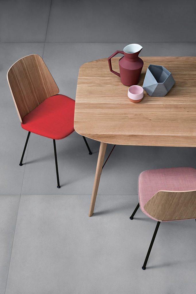 Two June chair with a cushioned seat one in pink and one in red; and natural wood backrest in a dining room.