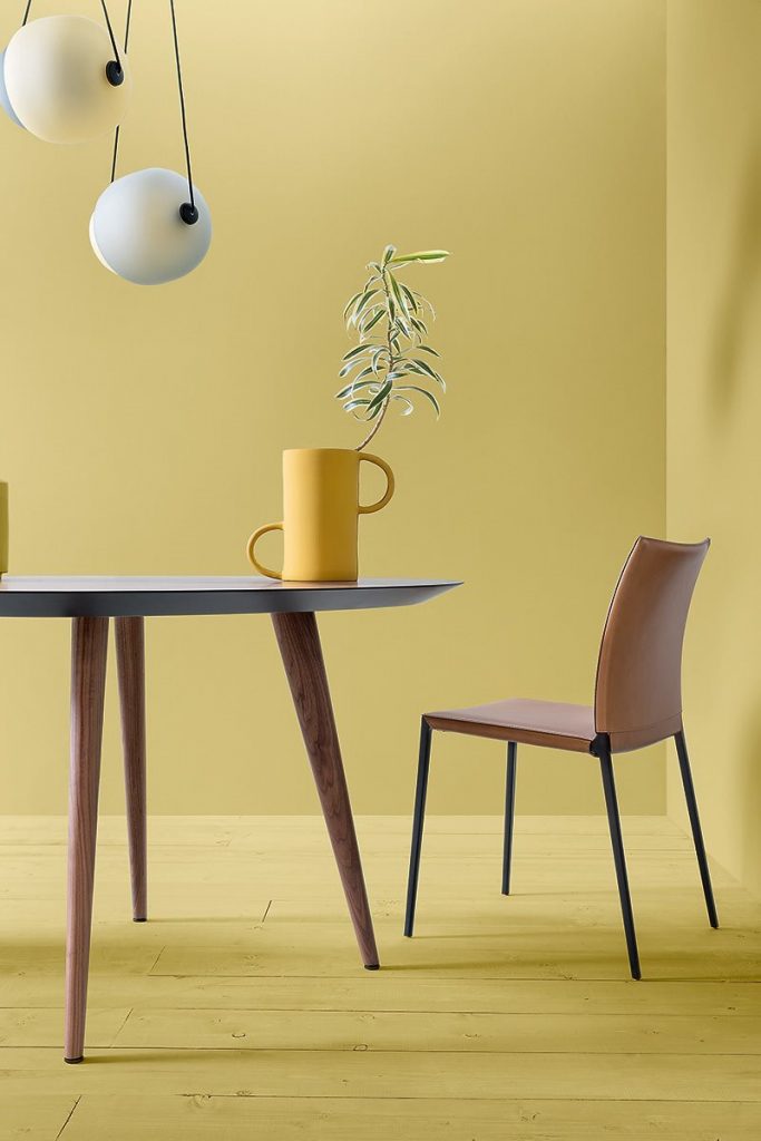 Lia chair in brown next to a table with a yellow wall in the background and a yellow floor