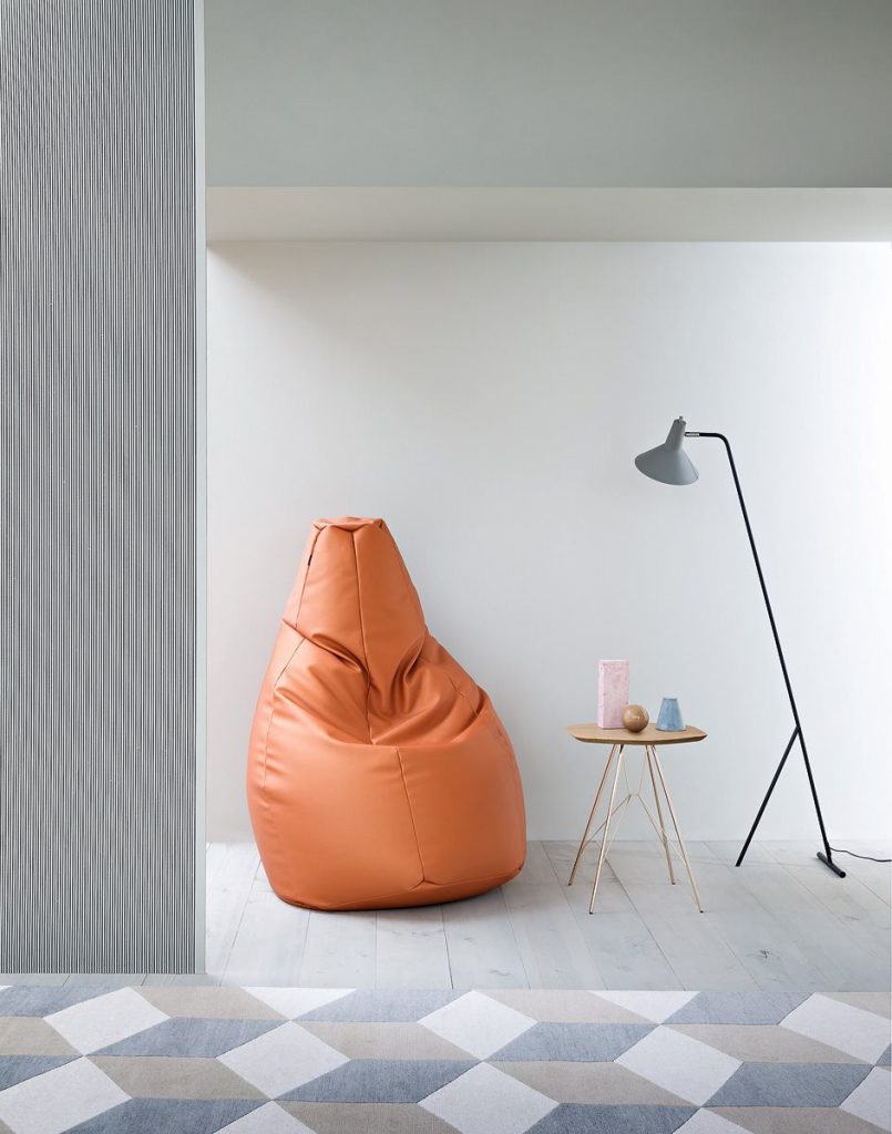 Sacco chair in orange in a white wall room with a lamp and small table next to the chair