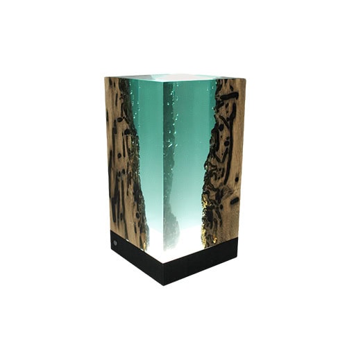 A sculptural lamp blending wood and resin with a glowing aqua core. Its striking depth effect mimics ocean waters, creating a warm ambient light and a captivating centerpiece.