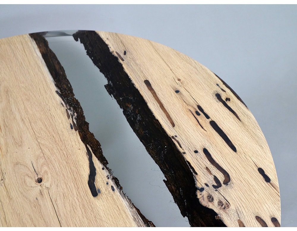 A round table that pairs natural oak planks with deep black resin, highlighting raw textures and organic voids. The seamless circular design balances modern craftsmanship with natural beauty.