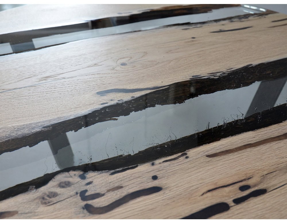 A round table crafted from natural wood and clear resin, highlighting organic cracks and patterns. Its smooth surface blends rustic textures with a sleek finish, creating a striking and modern centerpiece.