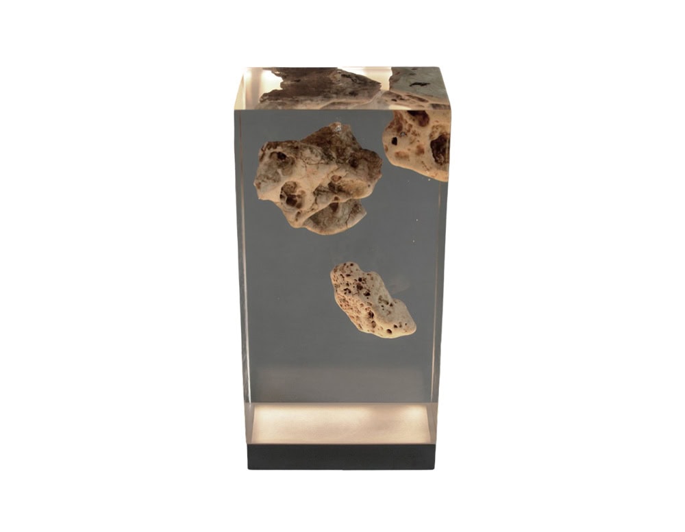 The Floating Karst Lamp features natural stone suspended in clear resin, illuminated from below to create the effect of rocks floating in light. Its sculptural design blends organic textures with a modern translucent base.