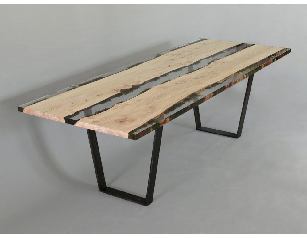 Handcrafted dining table with live edge wood slabs encased in clear resin and accented with natural moss inserts resting on sleek black metal legs.