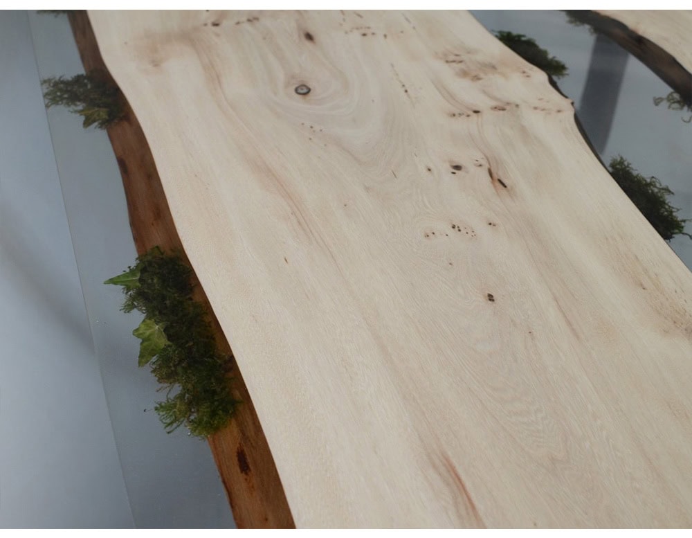 The Moss Table blends raw wood planks with embedded moss and transparent resin, creating a striking contrast of organic textures and modern design. Its steel legs provide sturdy support, making it a bold yet natural centerpiece.