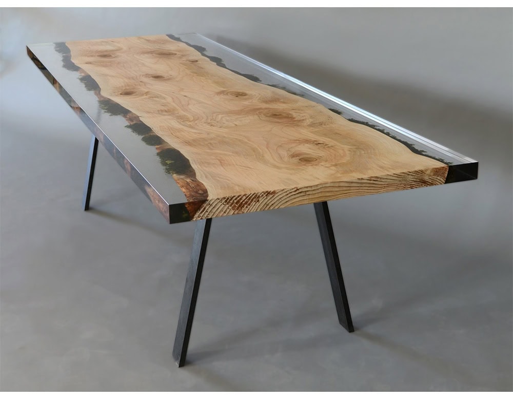 Moss Table reveals a broad natural wood surface framed by clear resin with moss details, bringing depth and contrast to its design. Resting on sleek metal legs, it combines raw organic beauty with a refined contemporary structure.
