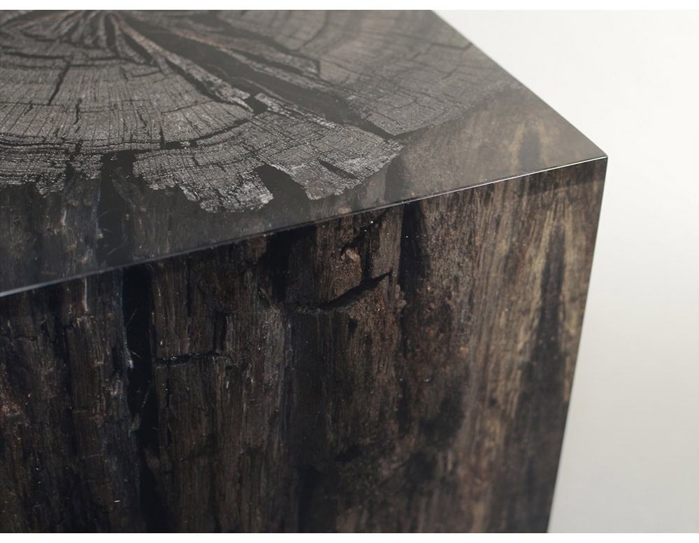 The Peatland Stool is a striking cube crafted from preserved peat encased in transparent resin, highlighting the raw textures of ancient wood with a modern, sculptural finish.
