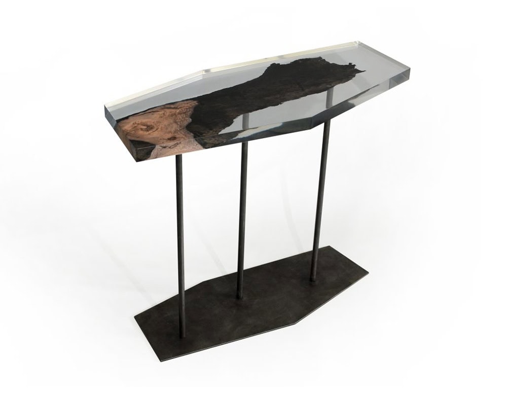 Wetland Fragment Console features a faceted resin top encasing a raw wood section, elevated by slender dark legs. Its design merges organic presence with sculptural elegance.