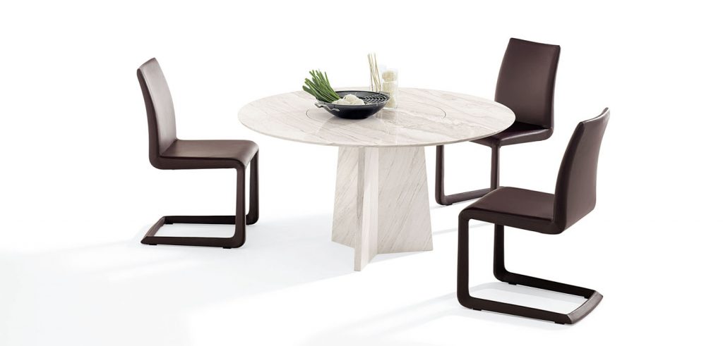 Round dining table with cone-shaped rotating inner plate in a cream color tone on a white background with chairs around