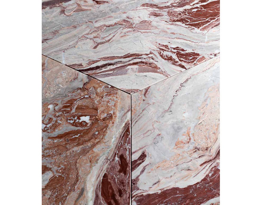 A close-up of a Giotto Outdoor Dining Table shows a surface with a swirling pattern of brown and white marble against a white background