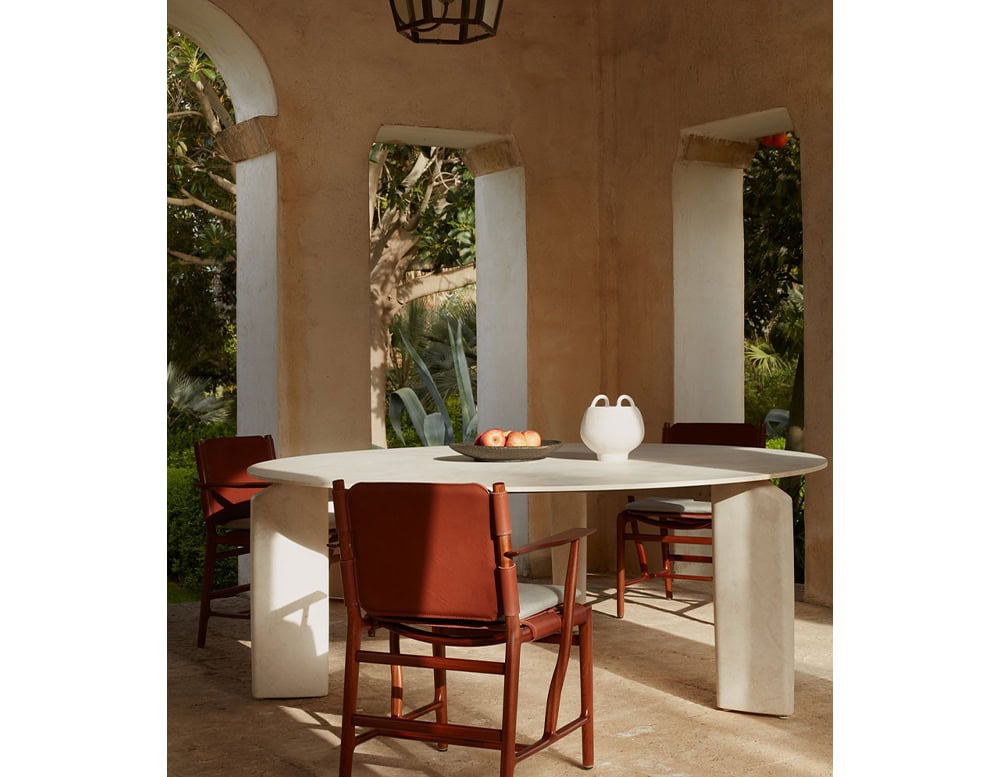 A Giotto Outdoor Dining Table with a rectangular white top and block legs is set with a red chair on a patio with arched openings and a hanging light