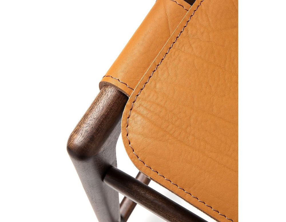 Closeup of Levante Stool. Structure in brown wood, seat in orange leather on a white background.