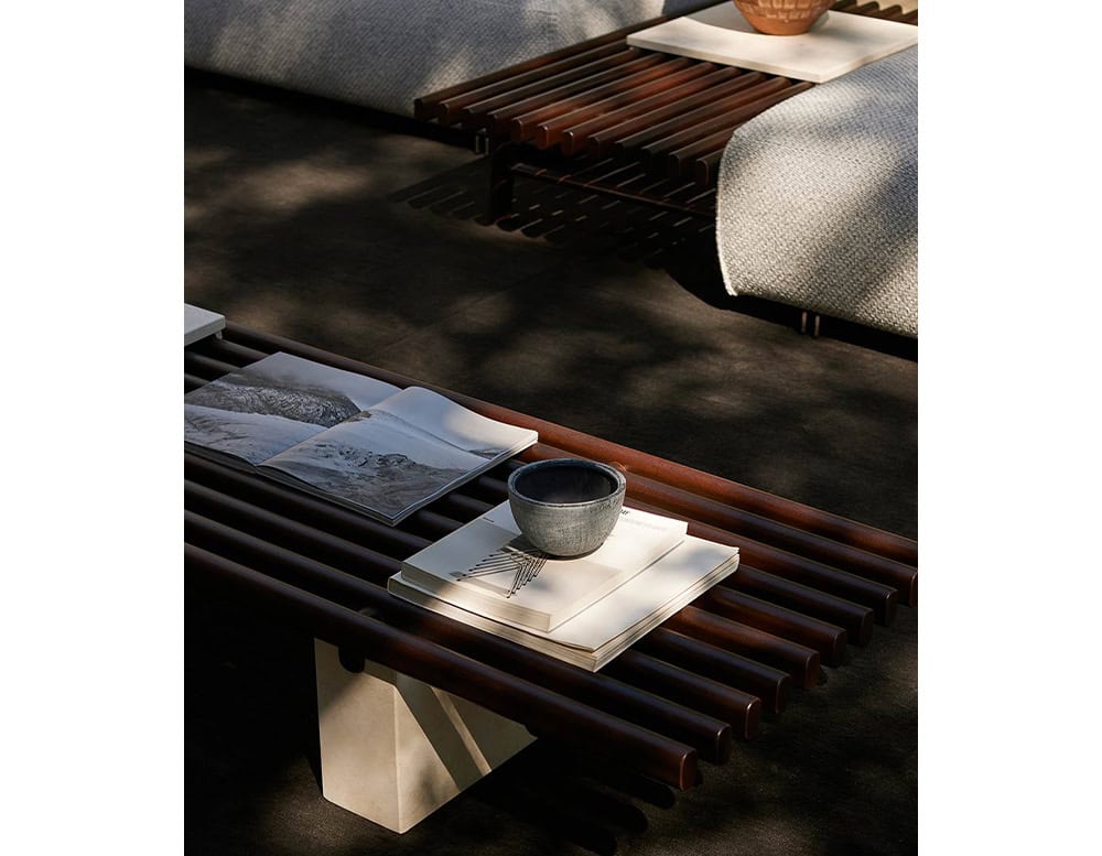 Panarea Coffee Table. Upper part made of brown wooden sticks and lower part is a block of yellow stone on a terrace.