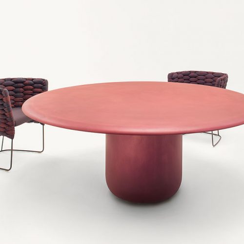 Gon Indoor Round Table, top and central leg in red steel with two chairs on a white background.
