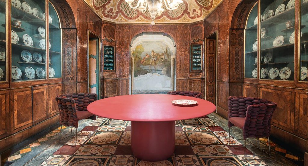 Gon Indoor Round Table, top and central leg in red steel in a dining room.