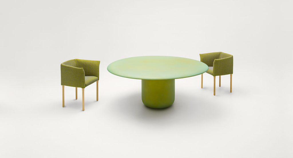 Gon Indoor Round Table, top and central leg in green steel with two chairs on a white background.