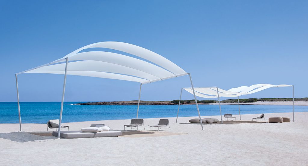 Two Ala shading structures and four legs made of white steel, shadding sail of white polyester fabric on a beach.