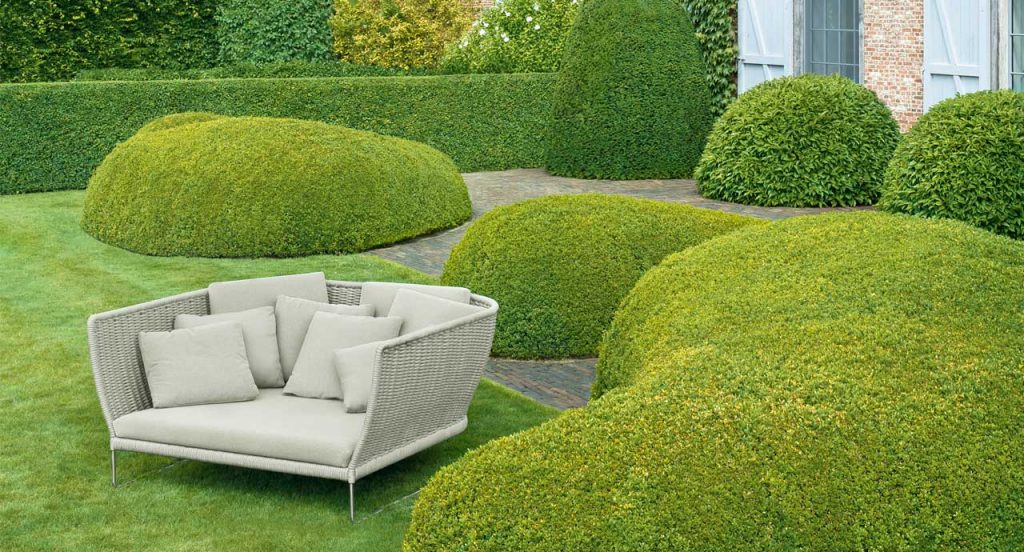 Ami Outdoor Sofa, structure and two legs in steel, structure upholstery in beige cord, white seat cushion in a garden.