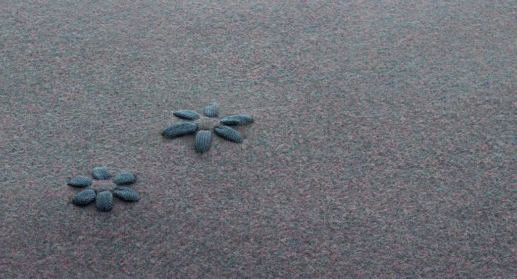 Asterisk rug made of gray felt with a blue floral design made of polyolefin cord.