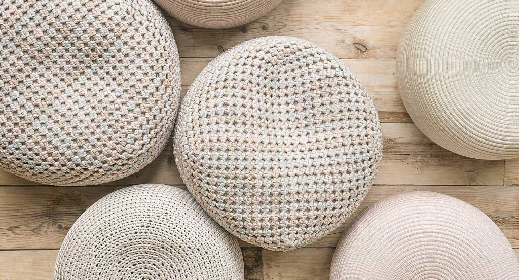 Two Berry poufs made of white woven upholstery on a natural wooden floor.