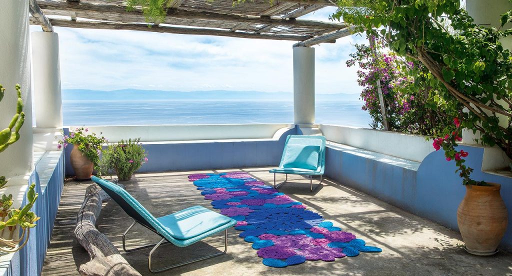 Crochet rug, flowers and leaves made of blue, pink and purple rope cord in a terrace.