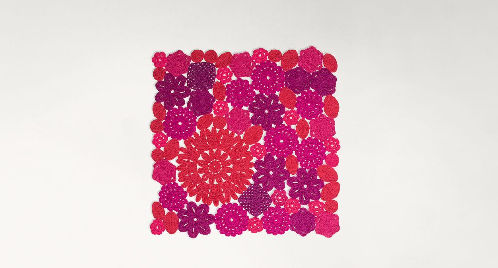 Crochet rug, flowers and leaves made of red,pink and purple rope cord on a white background.