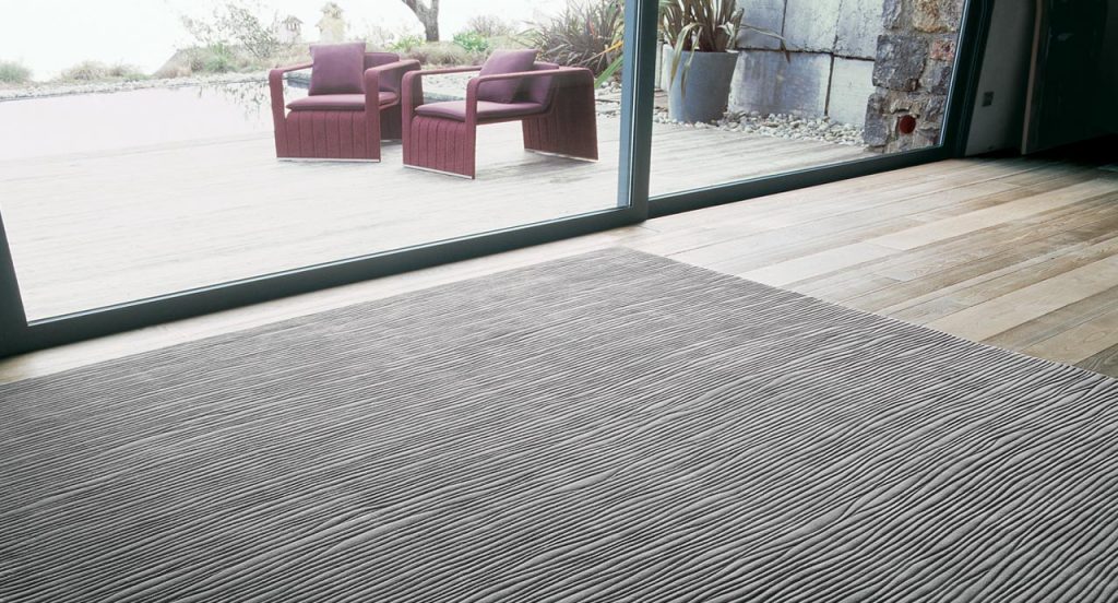 Deep rug made of grey irregular curved lines pattern on a brown floor.