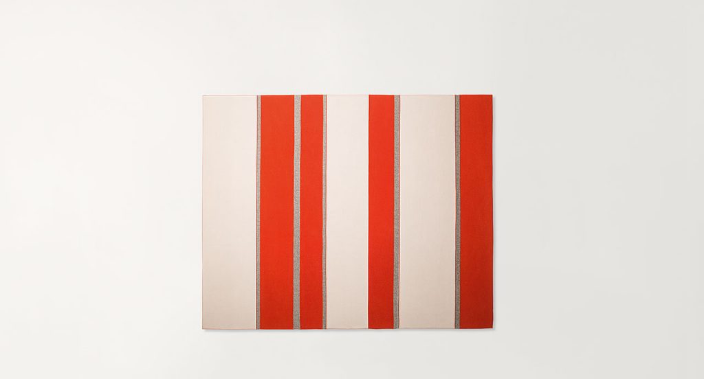 Fashion rug made of orange, grey and white felt strips on a white background.