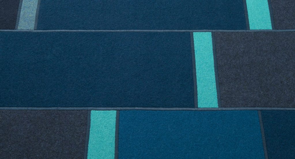 Fashion rug made of brown, blue and grey felt strips on a white background.