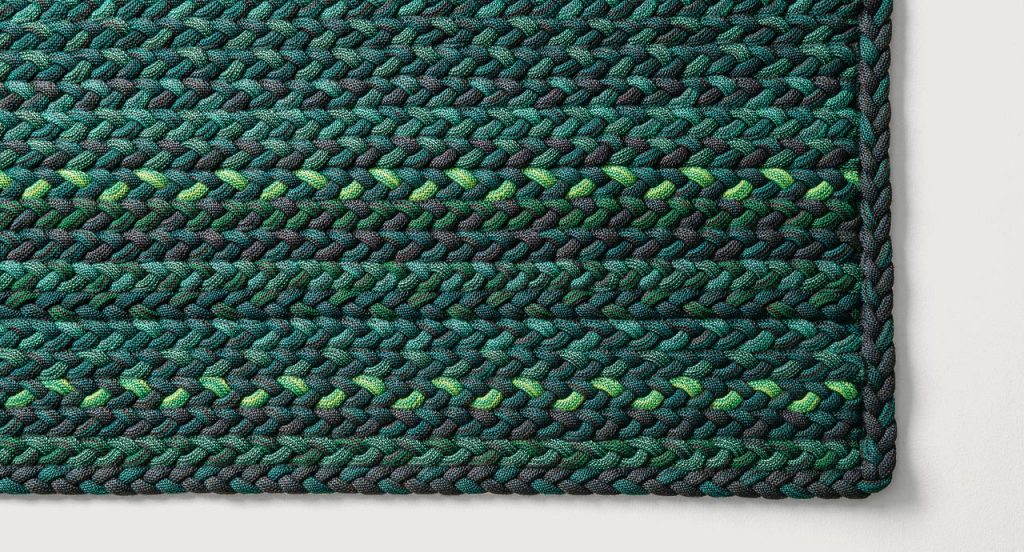 Flutti rug made of green and black braids of wool cords on a white background.
