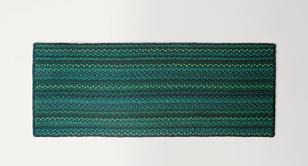 Flutti rug made of green and black braids of wool cords on a white background.