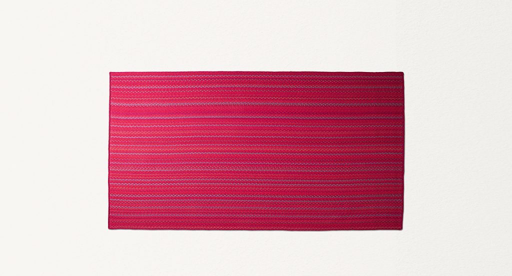 Flutti rug made of red and purple braids of wool cords on a white background.