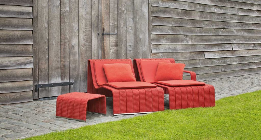 Two red Frame Chaises, upholstey of rope braids, seat pad and cushion in a garden.