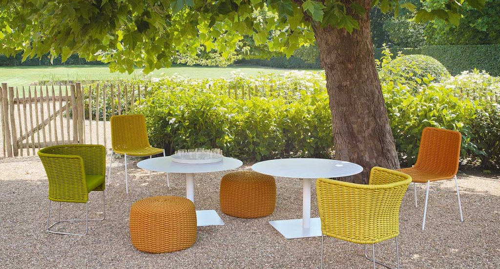 Two white Giro Outdoor Table tables, structure and central leg in steel, top in concrete in a garden.