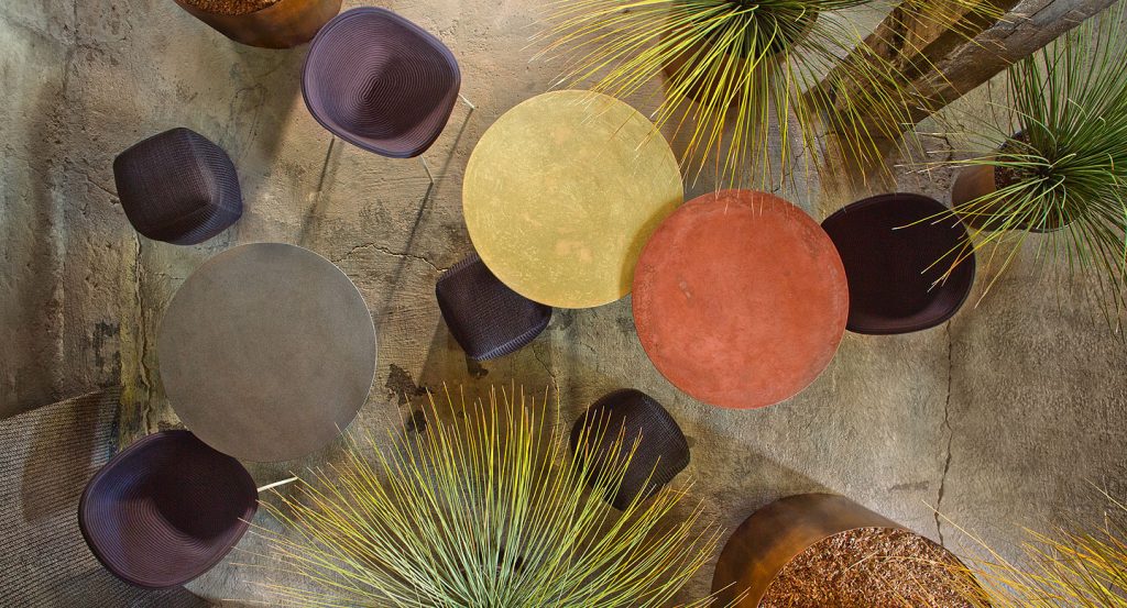 Three white Giro Outdoor Table tables, structure and central leg in steel, top in concrete, one in grey, one in yellow and one in orange in a dining room.