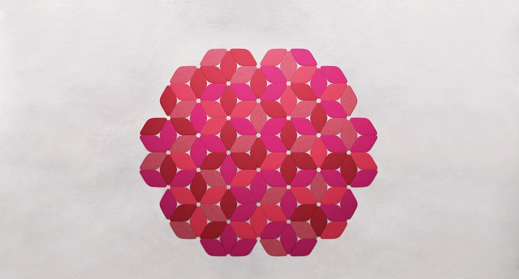 Kaleidoscope rug made of pink and red felt modules on a grey background.