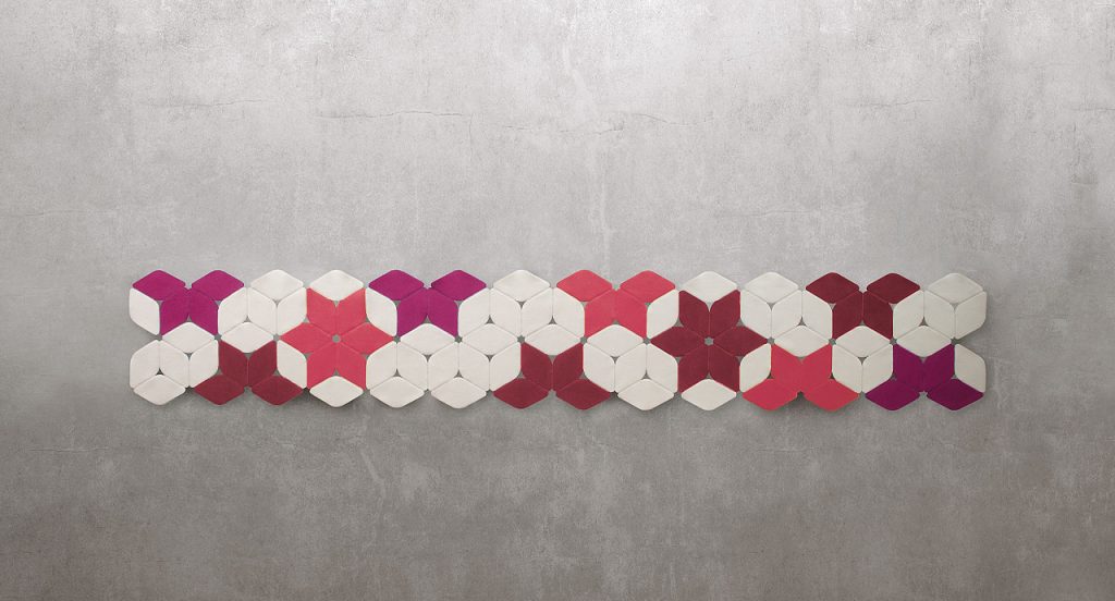Kaleidoscope rug made of pink, white and red felt modules on a grey background.