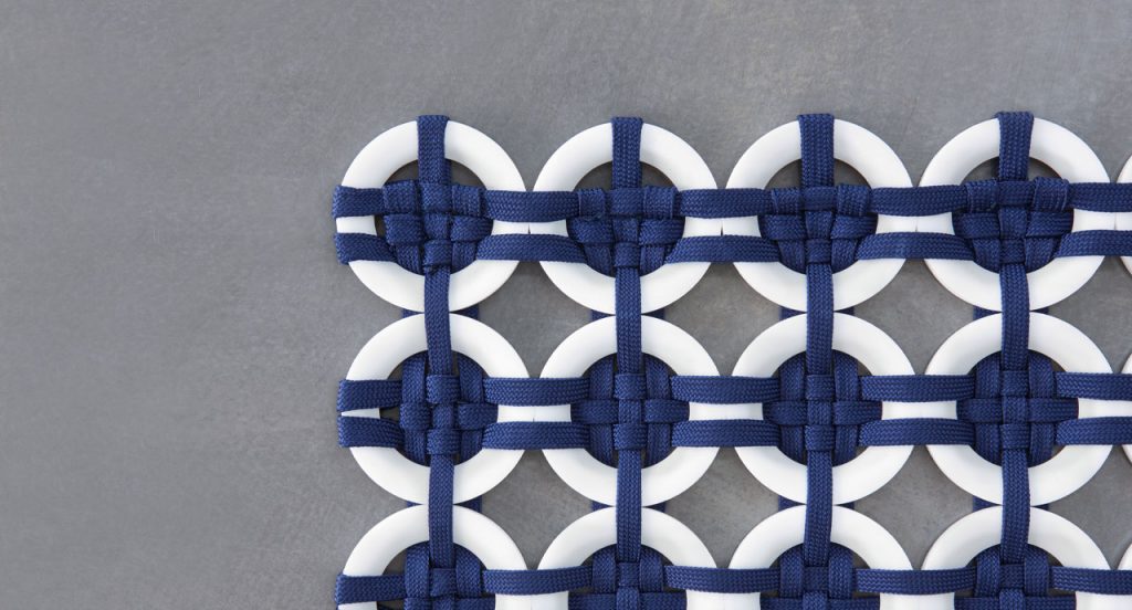Loom rug made of white plastic rings and blue rope braids on a gray background.