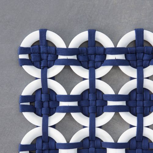 Loom rug made of white plastic rings and blue rope braids on a gray background.