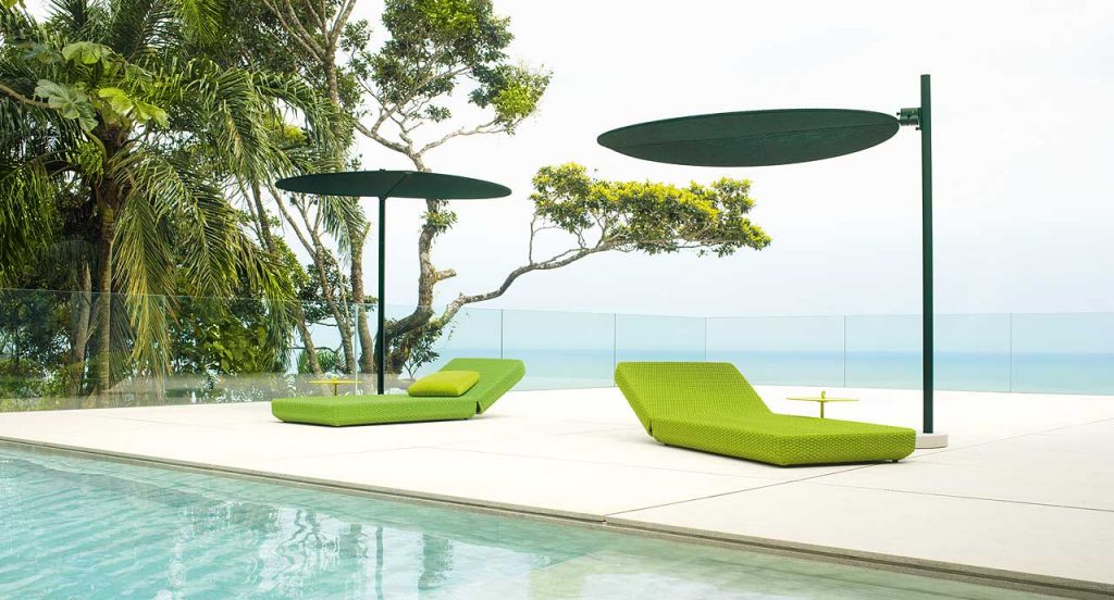 Two green Ombra sunshades top made of two polyester semi circles, leg in aluminum next to a pool.